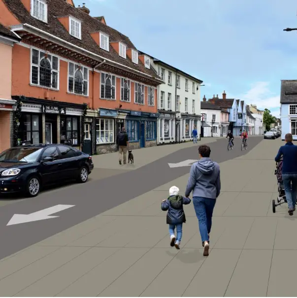 Pedestrians in a street with a car by shops.