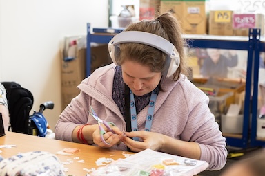 A person with learning disabilities sitting doing crafts listening to headphones.