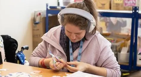 A person with learning disabilities sitting doing crafts listening to headphones.