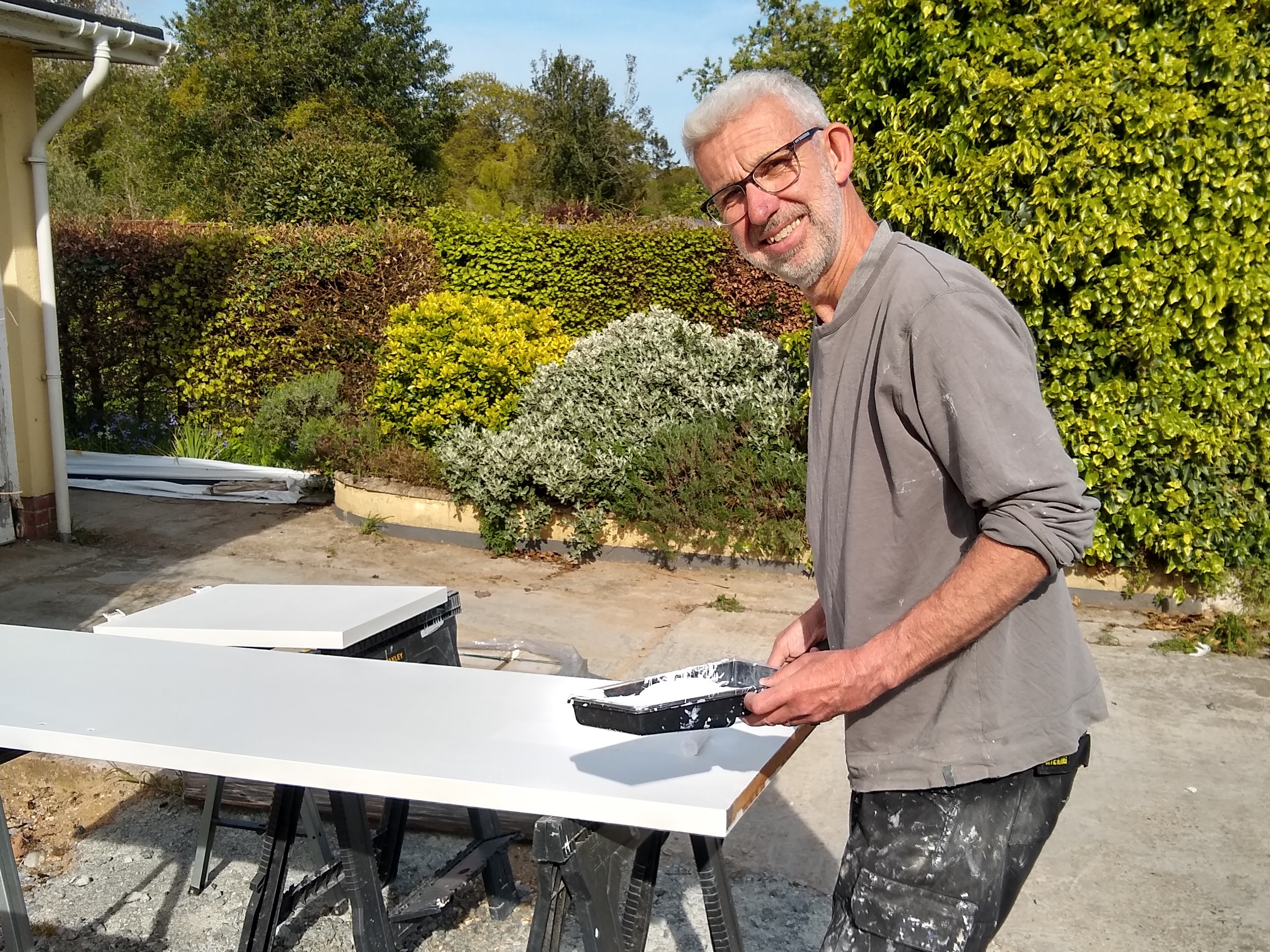 Steve is working outside using a roller and paint to paint a block of wood