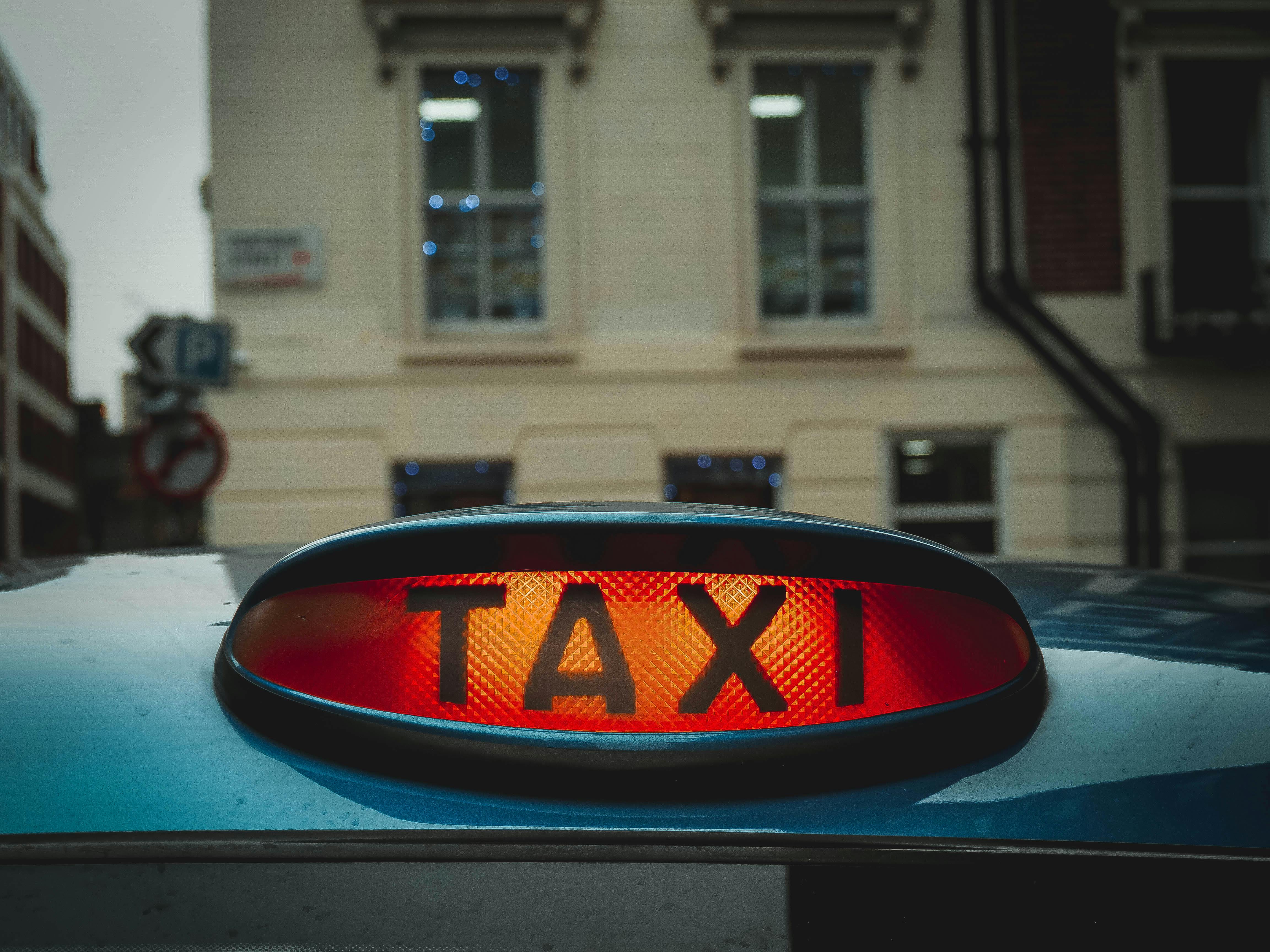 A lit up taxi sign sitting on the roof of a vehicle.