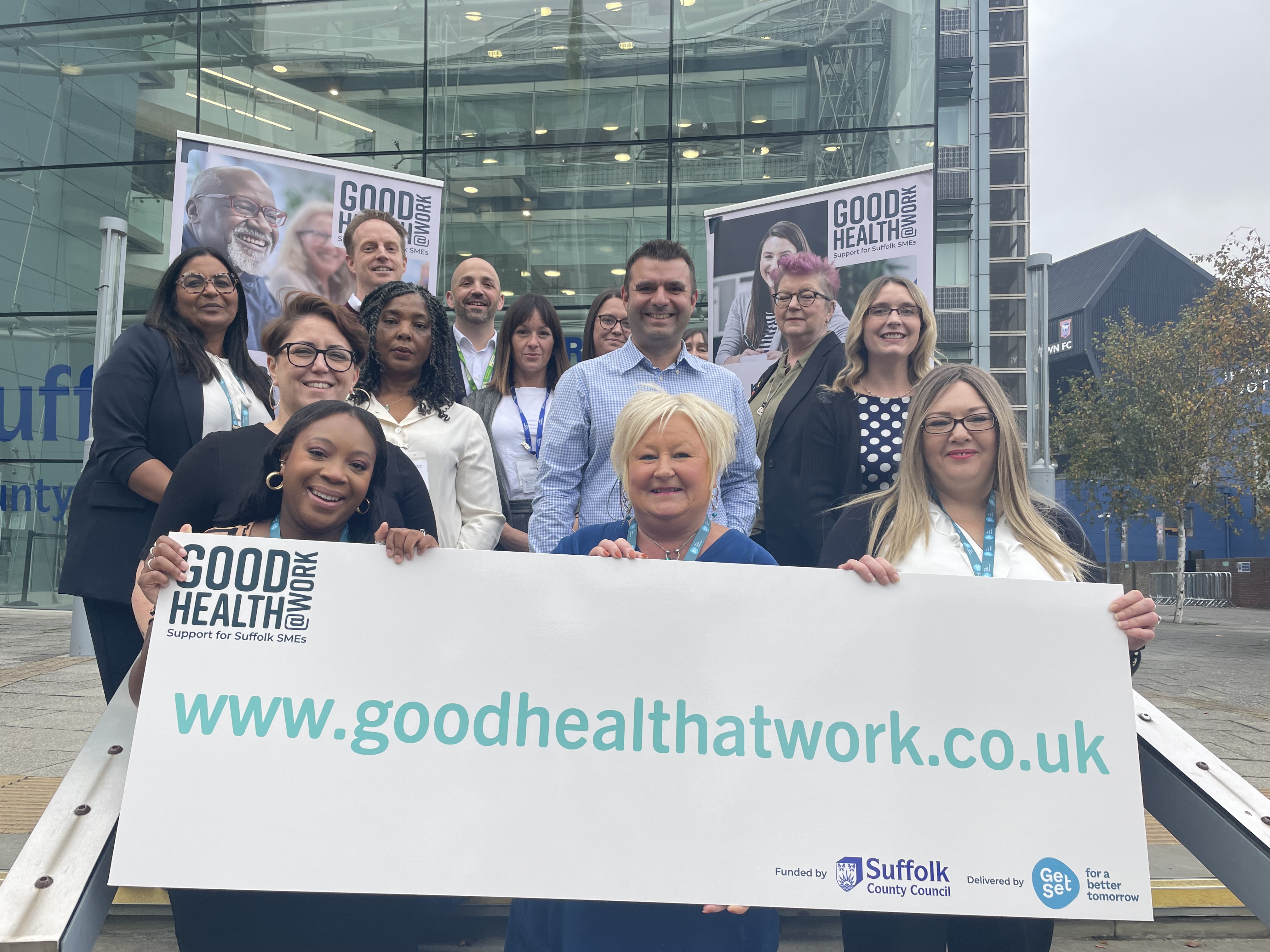 Group standing holding a sign saying good health at work.