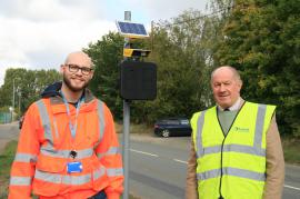 Two men in high visibility jackets stand in front of the ANPR device 