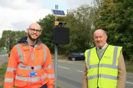 Two men in high visibility jackets stand in front of the ANPR device