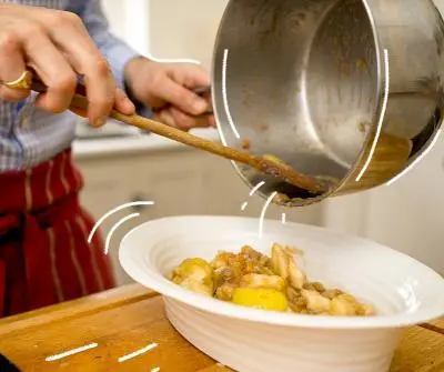 Person pouring food into dish with saucepan