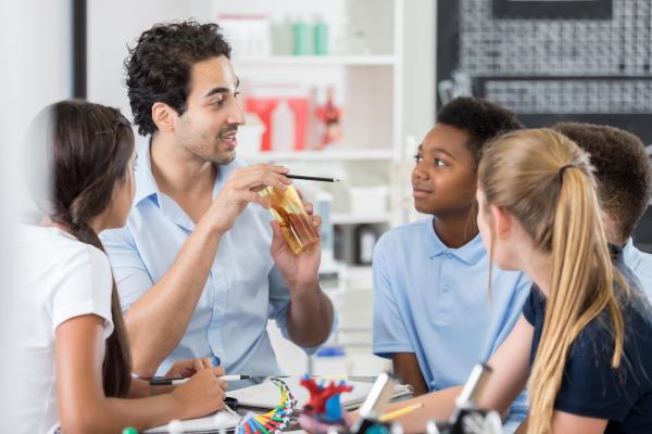 A teacher in a classroom is supporting 3 young students