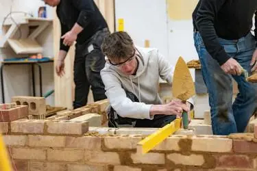 A young man is using a spirit level whilst constructing a small brick wall.