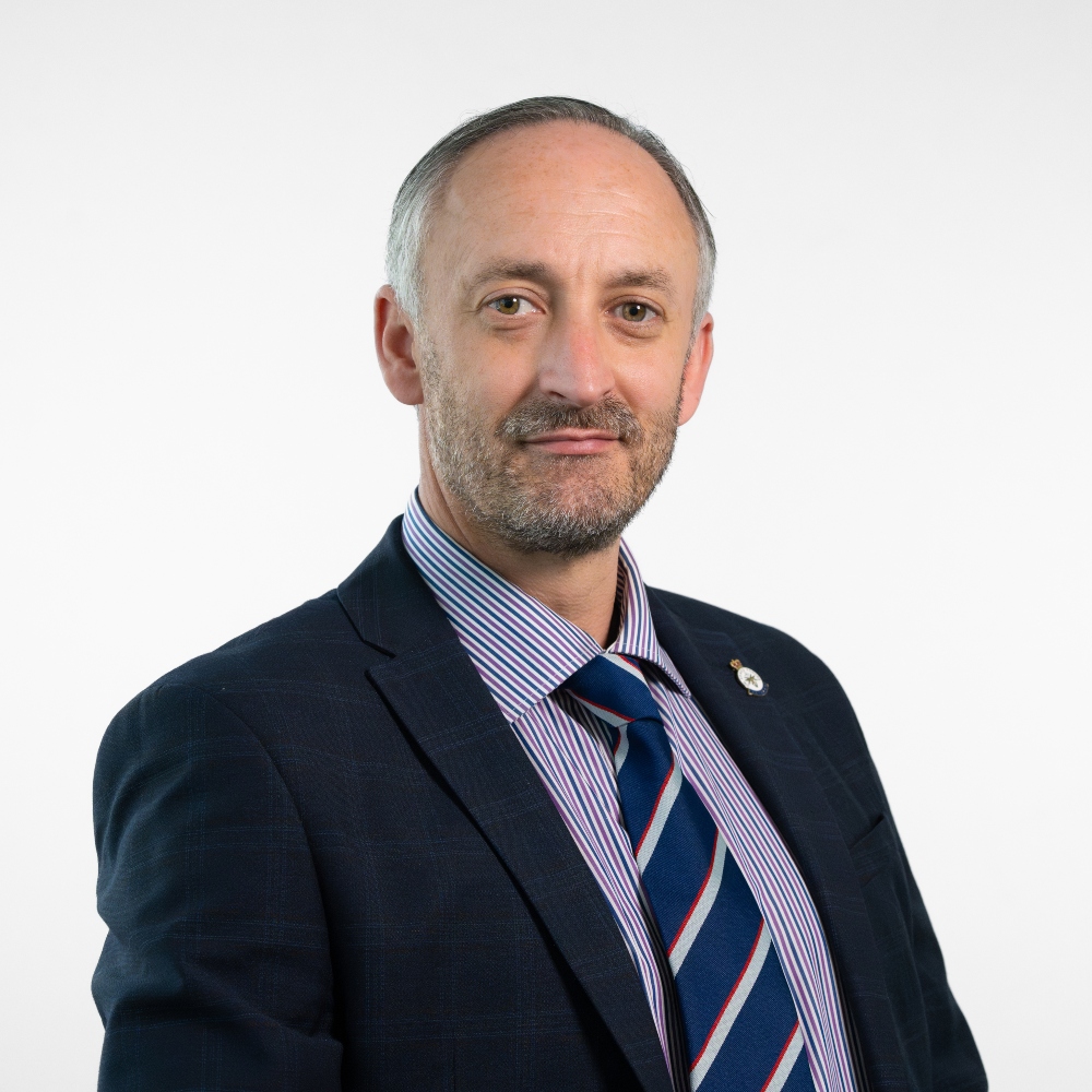 Councillor James Patchett wearing a blue jacket with a blue, red and white striped shirt and tie smiling.
