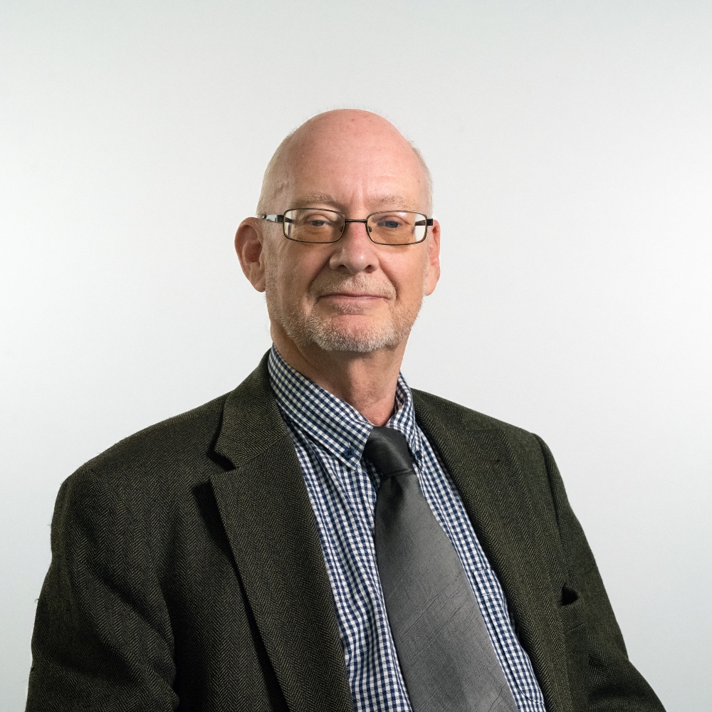 Councillor John Nunn wearing a dark grey jacket checked blue and white shire and grey tie smiling