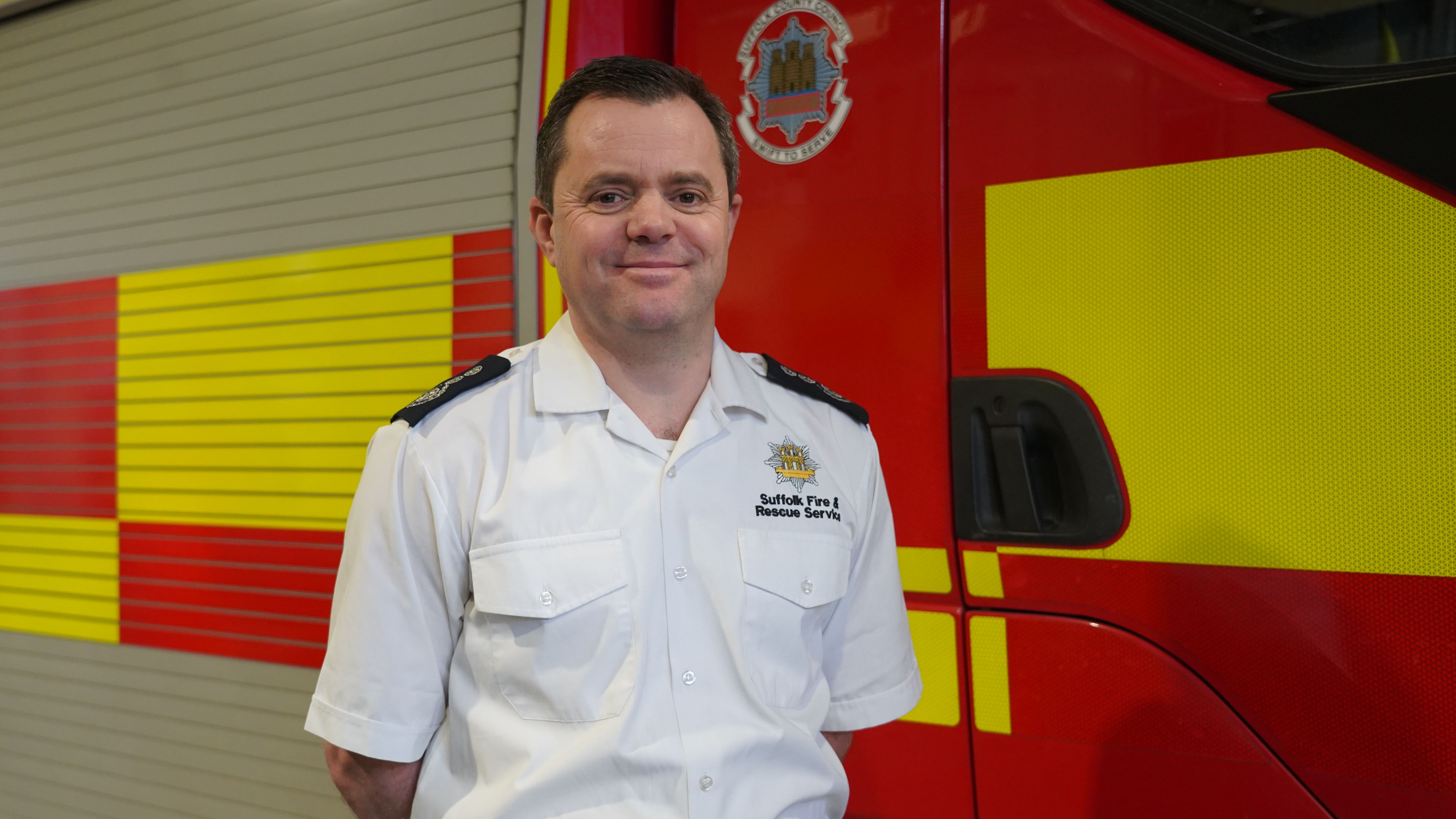 Smiling fire officer stands in front of fire engine