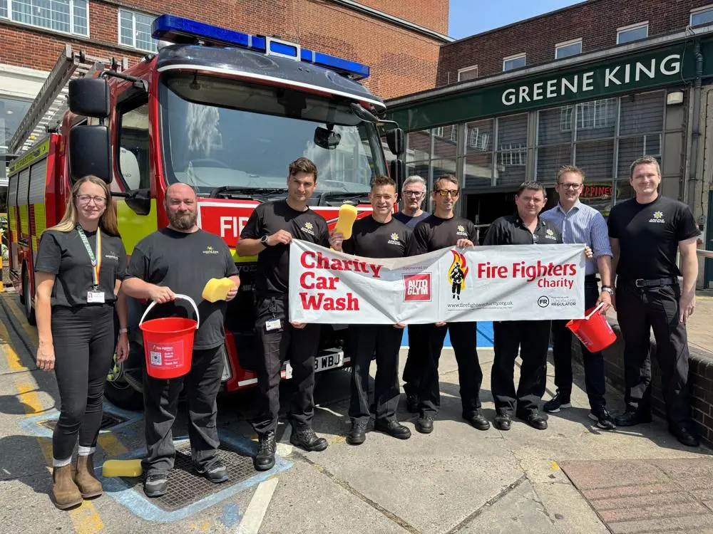 Firefighters and staff from Greene King pose outside Greene King in front of a fire engine holding a banner launching the charity car wash
