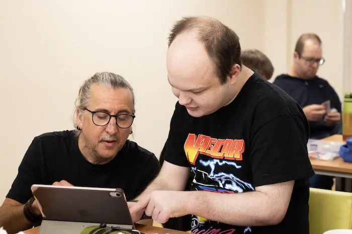 A person with learning disabilities looking at a tablet with a person supporting them