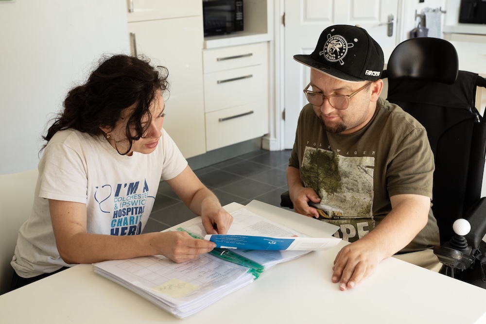 Two people sitting discussing some forms. One person is in a wheel chair and has learning disabilities. 