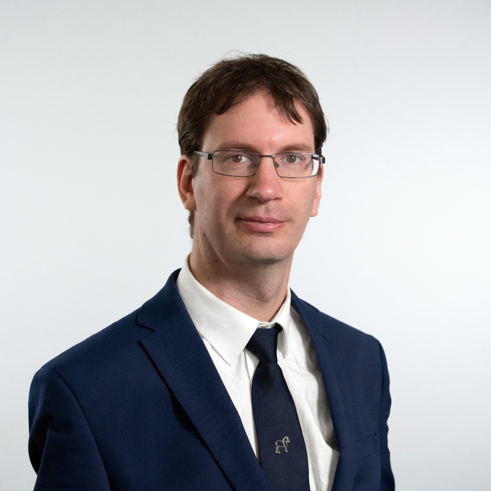 Councillor Luke O'Brien wearing a dark blue jacket with white shirt and dark blue tie smiling