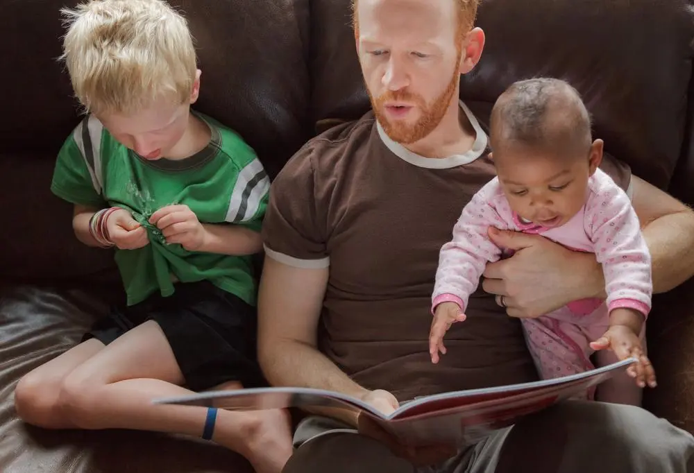 A man is sitting on a sofa reading a book to two children.