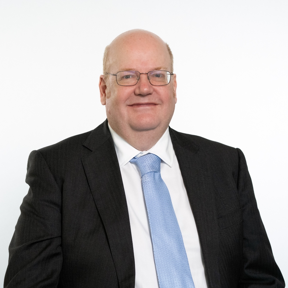 Councillor Martin Cook wearing a dark grey jacket with a white shirt and pale blue tie smiling