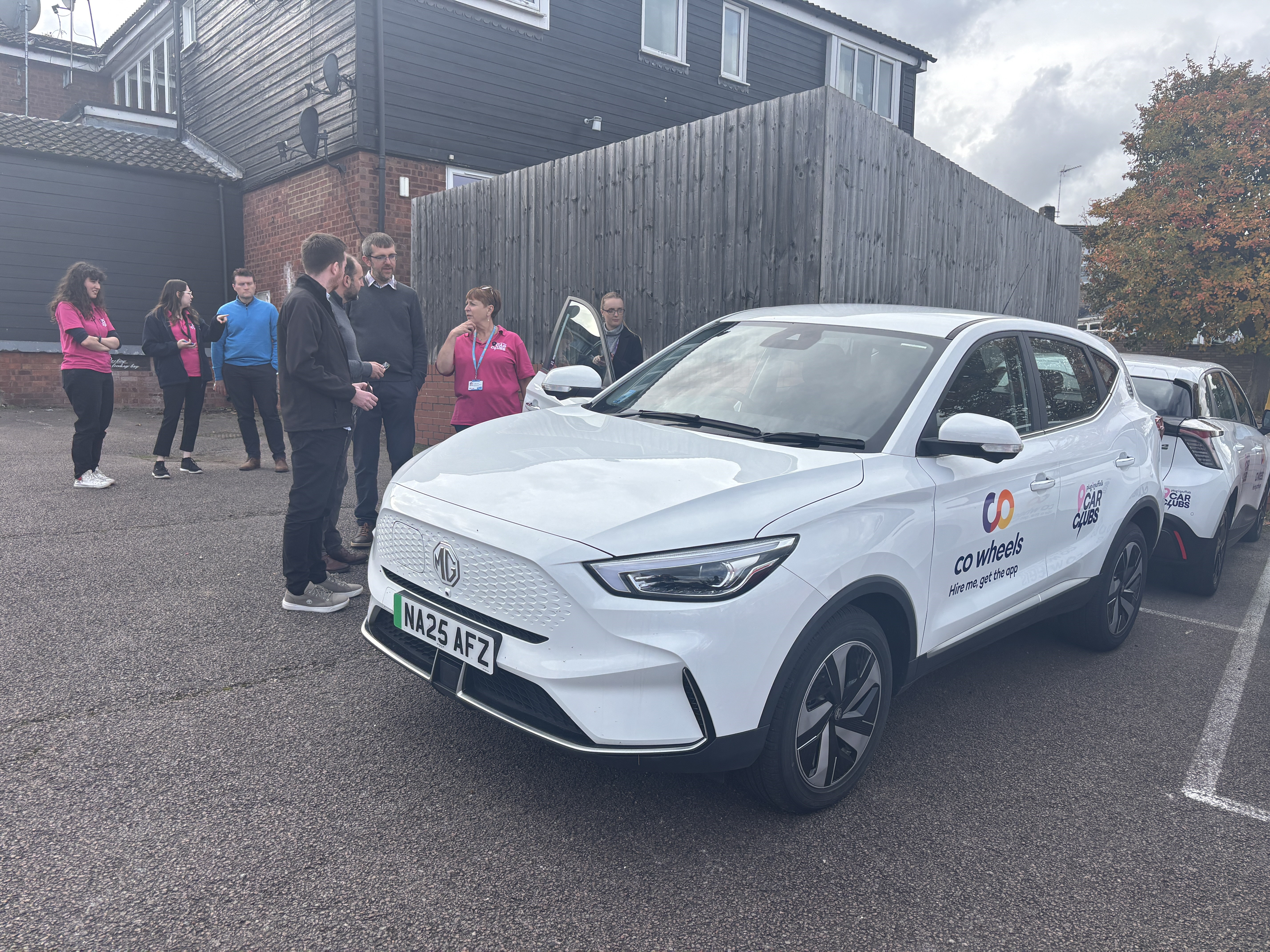 A group of councillors and officers having a discussion next to a car club vehicle. The car is a white electric MGZS.
