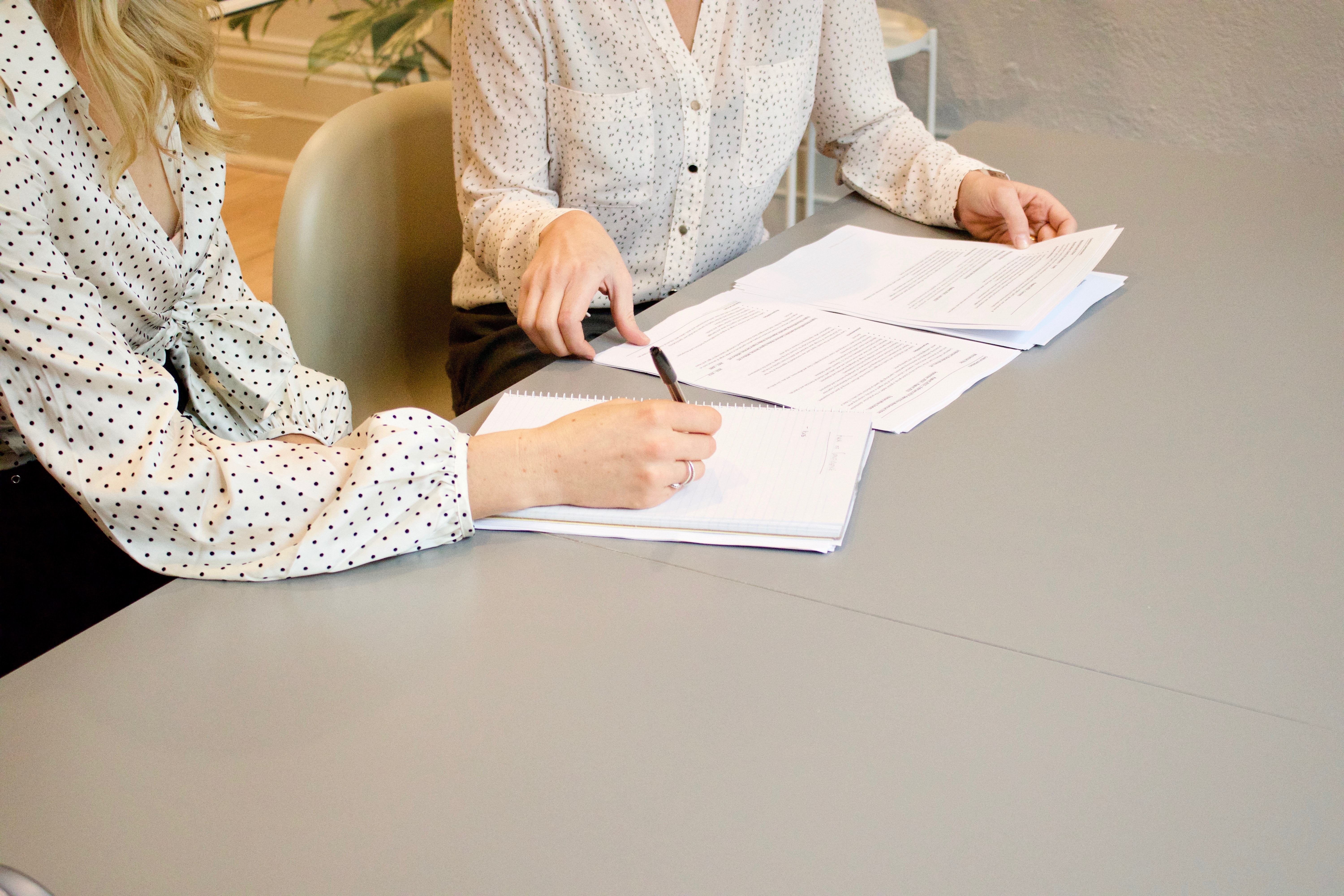 Two women in an office working together on a project, writing in a notepad