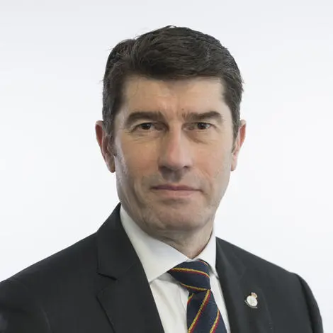 Image of Mick Fraser, Councillor wearing a dark suit jacket, white shirt and stripped tie wearing a veterans pin badge