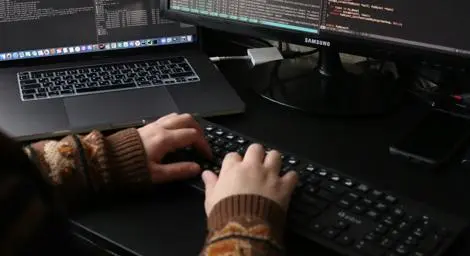 view of person's hands using a keyboard entering data which is displayed on two monitors