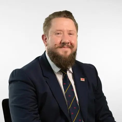 Councillor Brobyn wearing a navy jacket white shirt and blue, red and yellow patterned tie smiling.