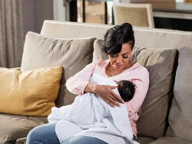 Mother sitting on a sofa breastfeeding her baby.