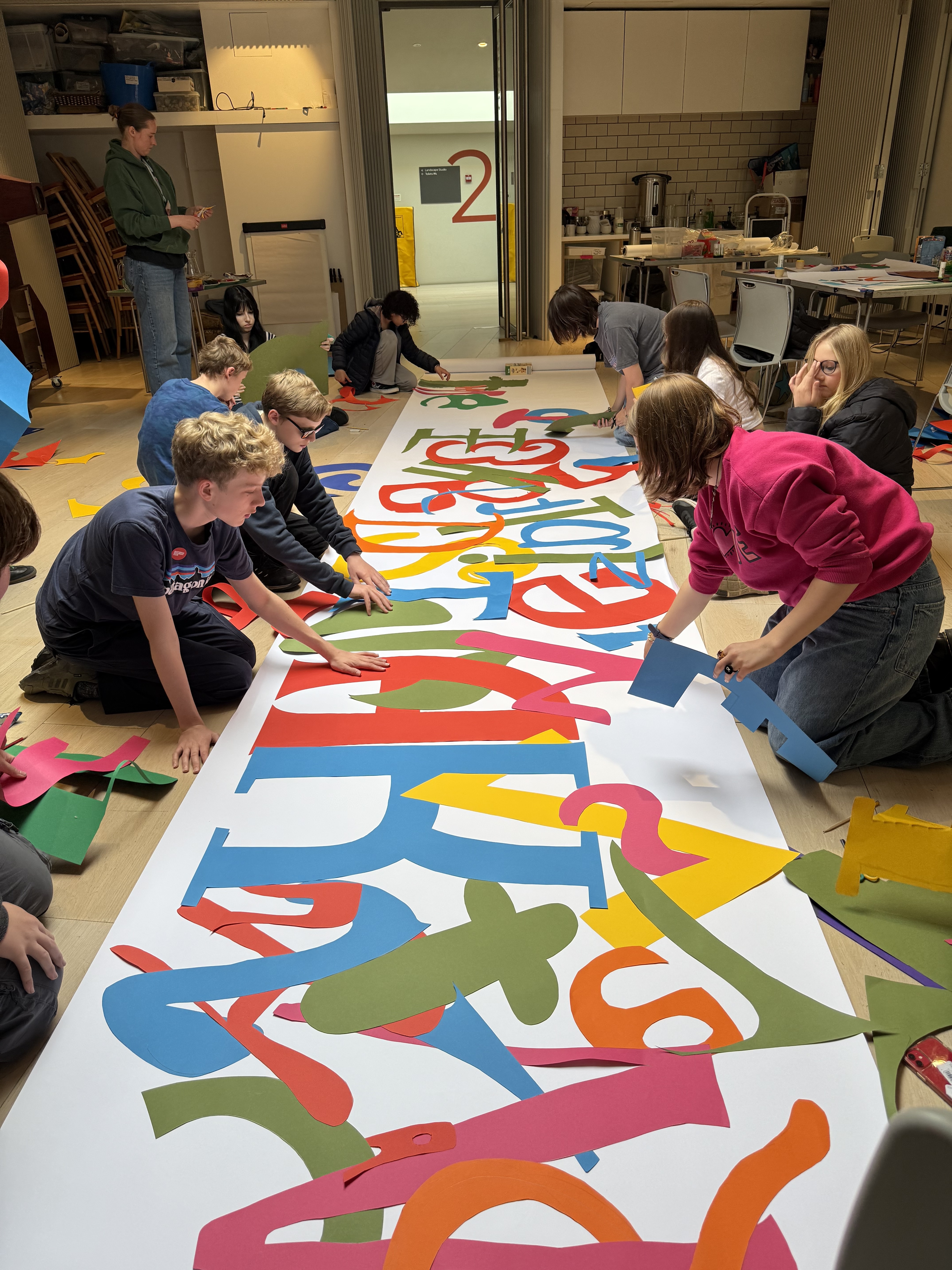 Several young people on the floor creating a large print of shapes and colours 