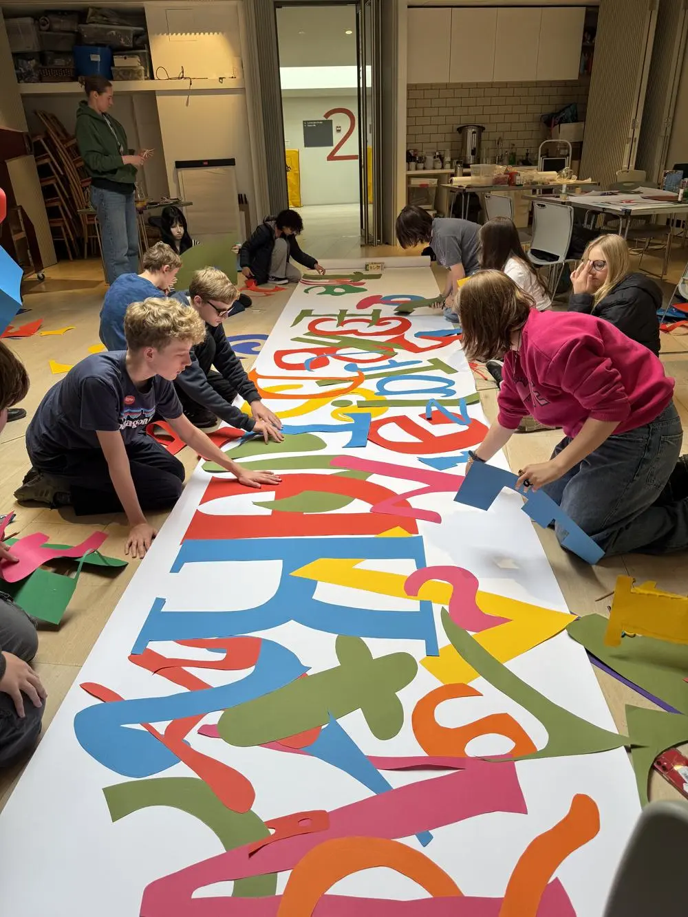 Several young people on the floor creating a large print of shapes and colours