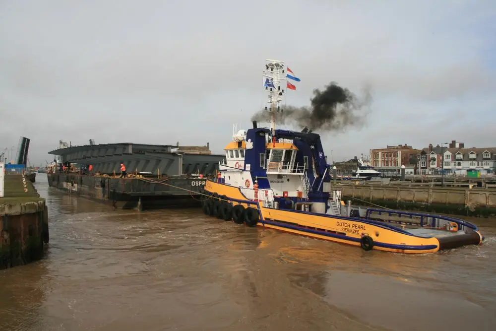 With a tugboat at either end the barge is manoeuvred into position to navigate through the Bascule Bridge. 