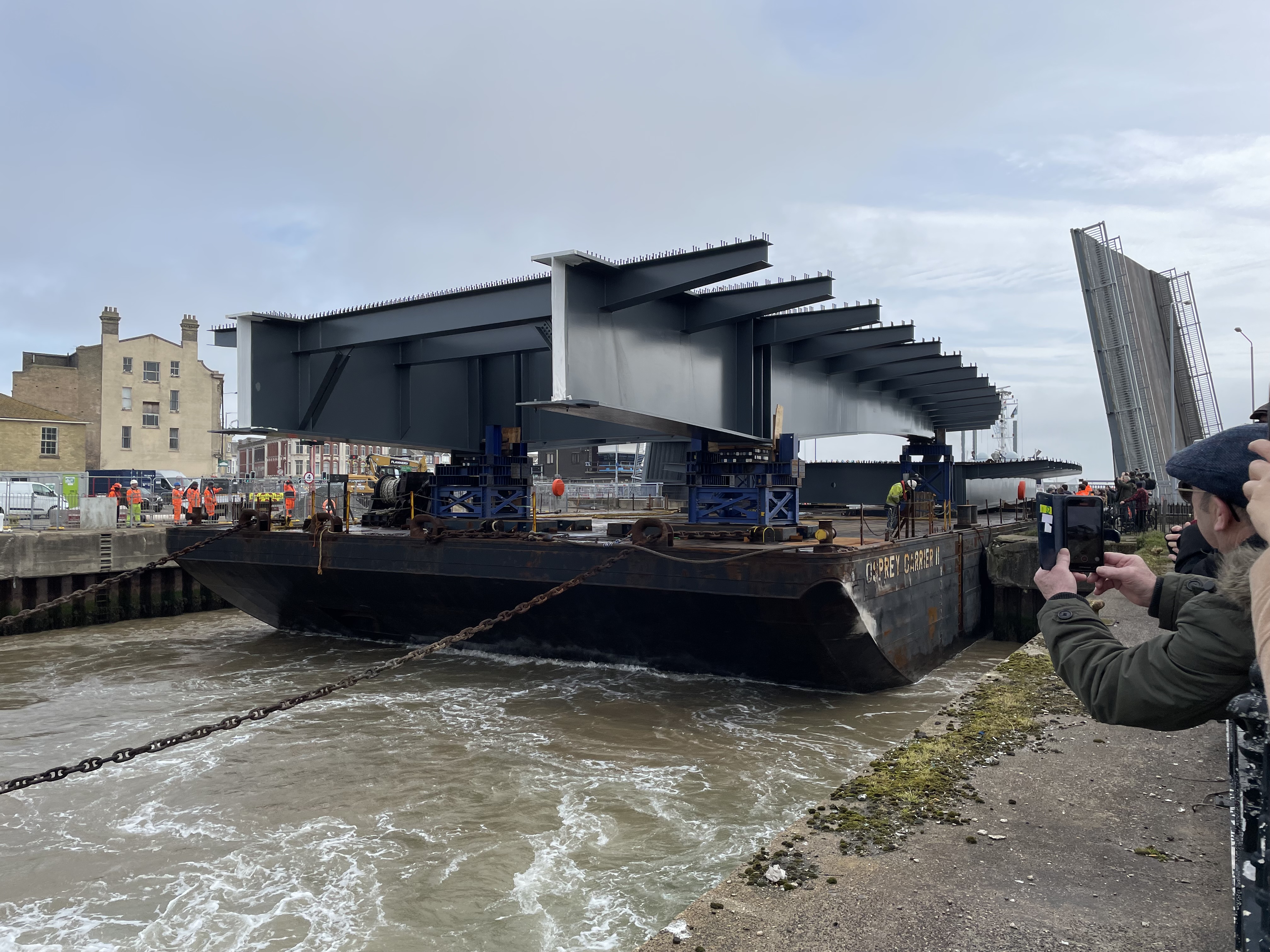 Crowds look on from the quayside as the barge eases through the Bascule Bridge.