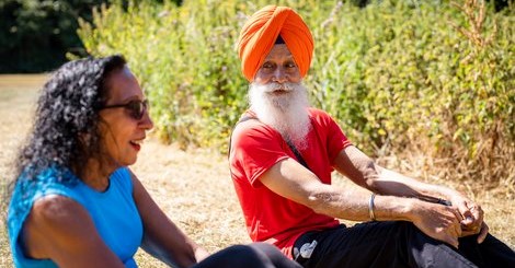 Old Sikh man exercising and doing sit ups with a woman in a park on a sunny day