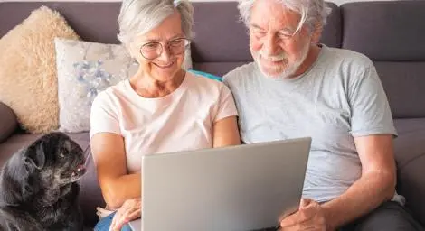 Older woman and man looking at a laptop screen with a dog next to them