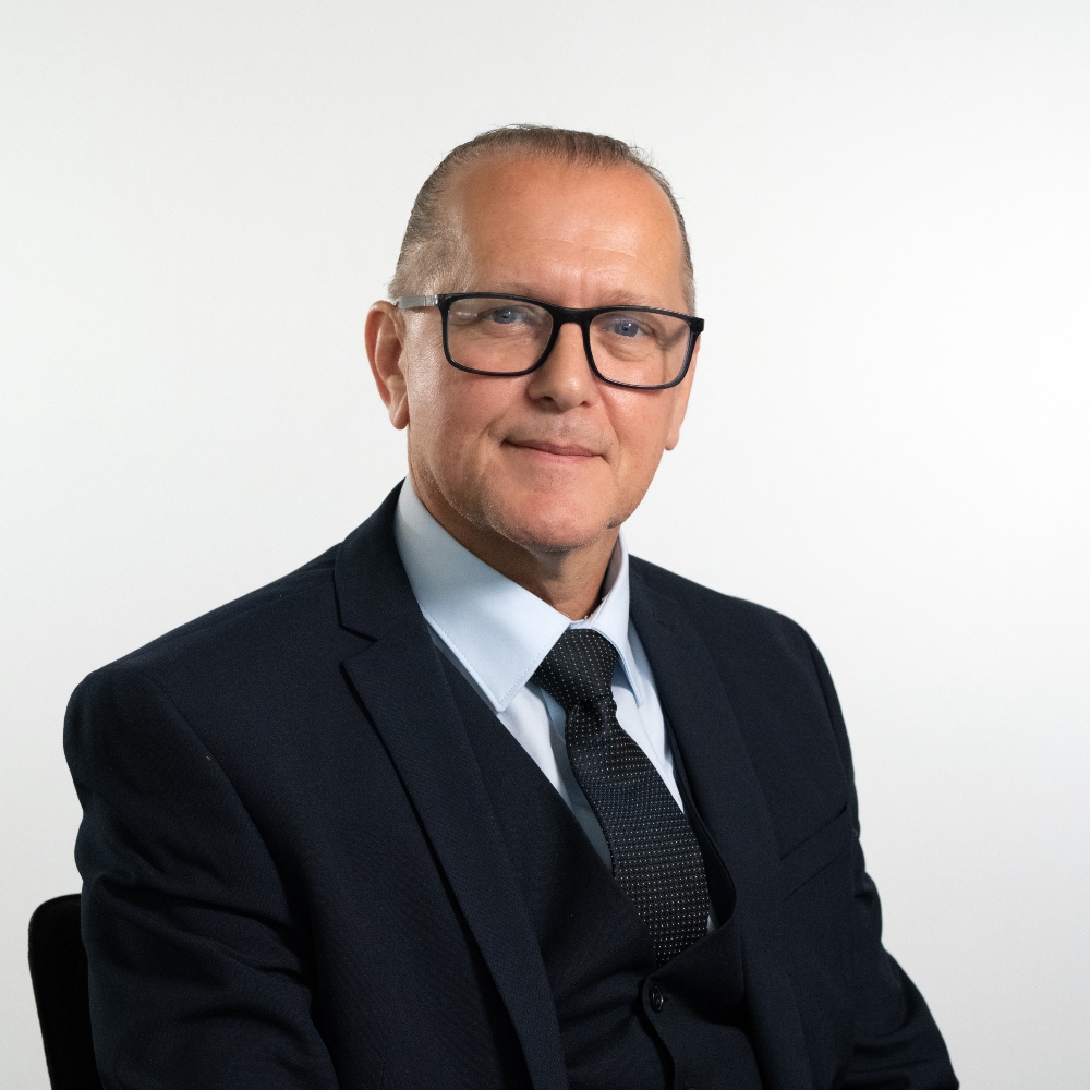 Councillor Paul Littman wearing a dark blue suit with white shirt and dark blue tie and black framed glasses smiling