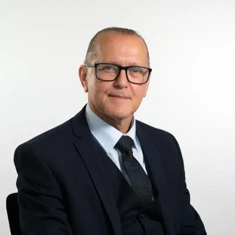 Councillor Paul Littman wearing a dark blue suit with white shirt and dark blue tie and black framed glasses smiling