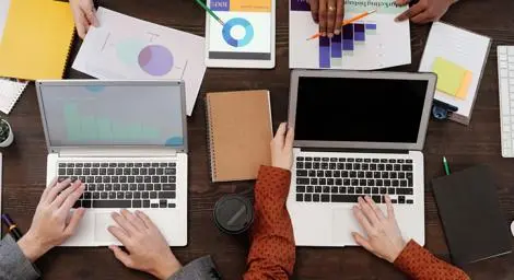 overhead view of two open laptops with the hands of a number of people using keyboards for reviewing data charts