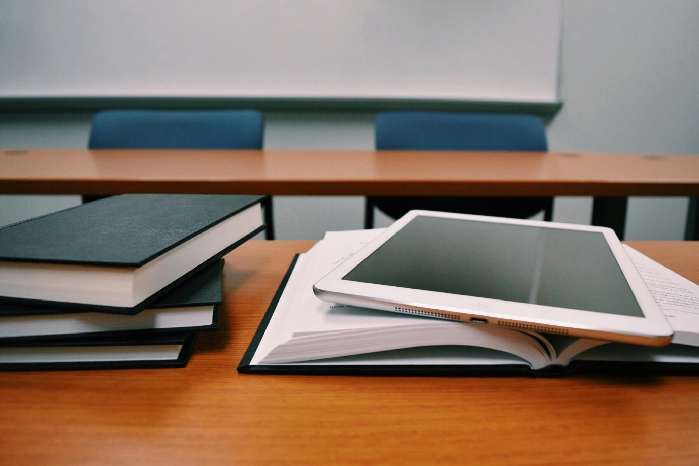 books stacked and laying open with an ipad sitting on top of the open book