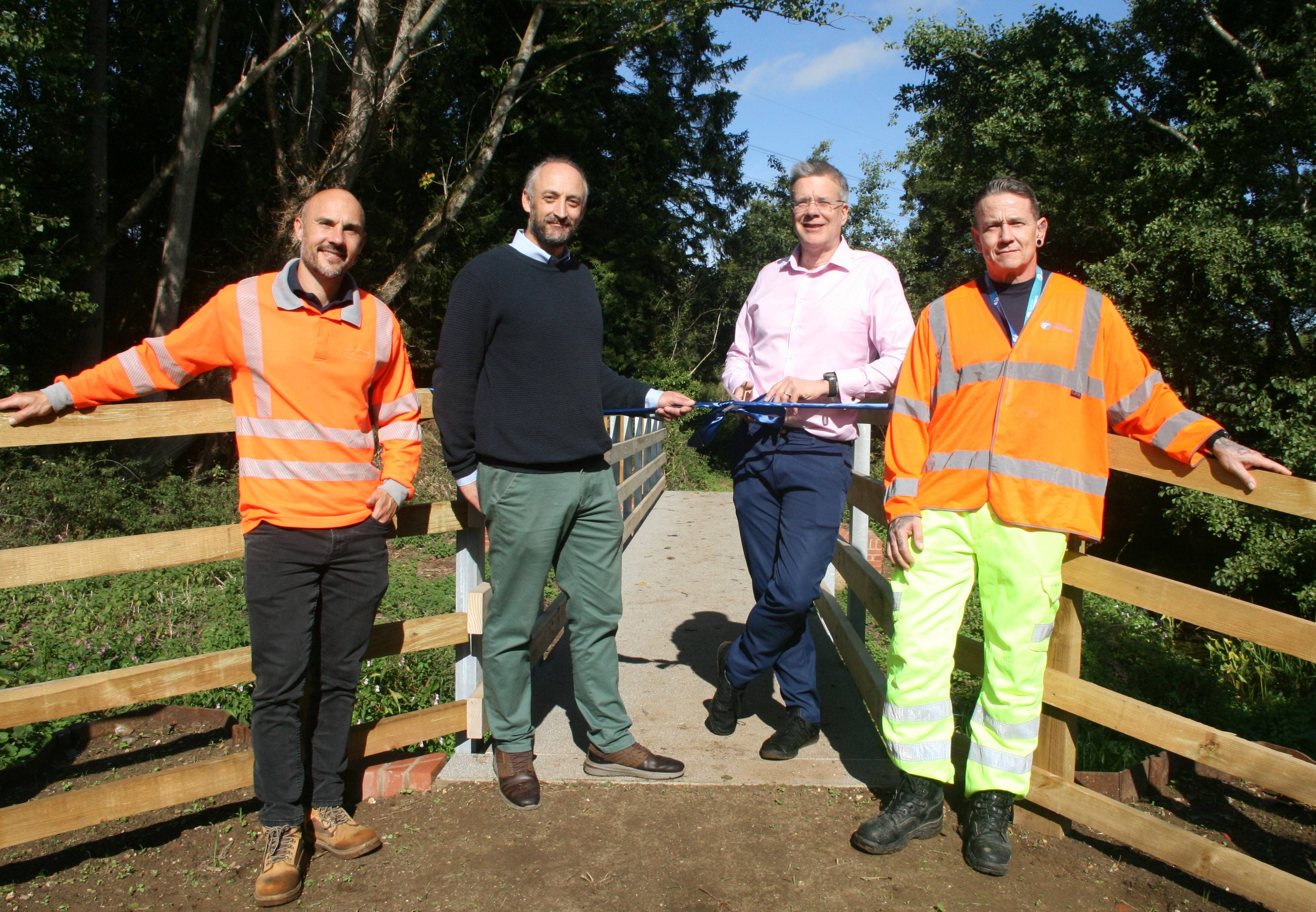 Two men in working clothes and two councillors cut the ribbon on the new bridge