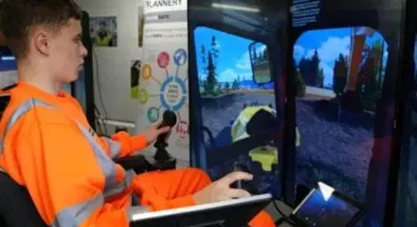 A man in an orange hi-vis jacket is using a simulator of a digger