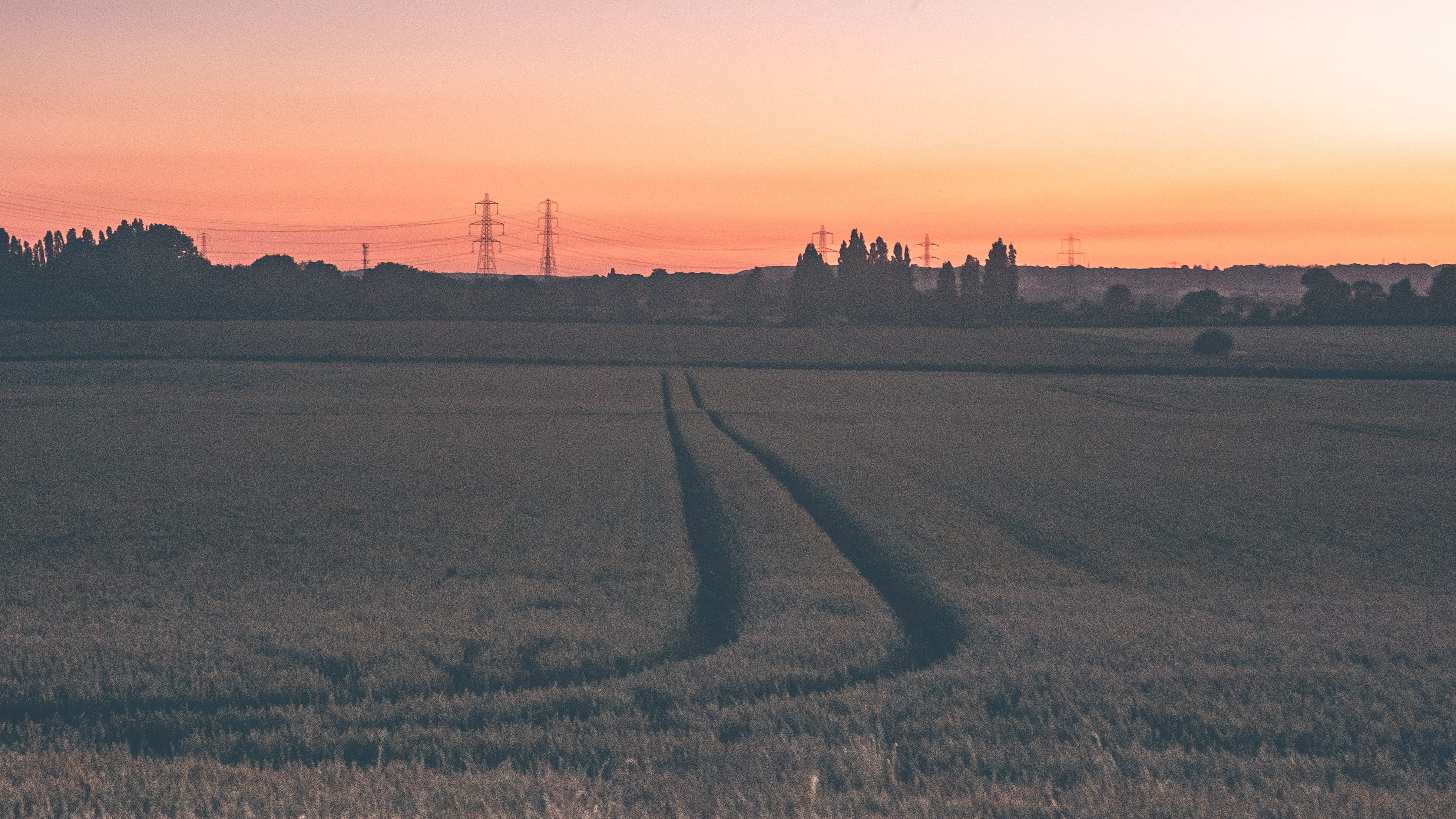 a field at sunset with pylons on the horizon