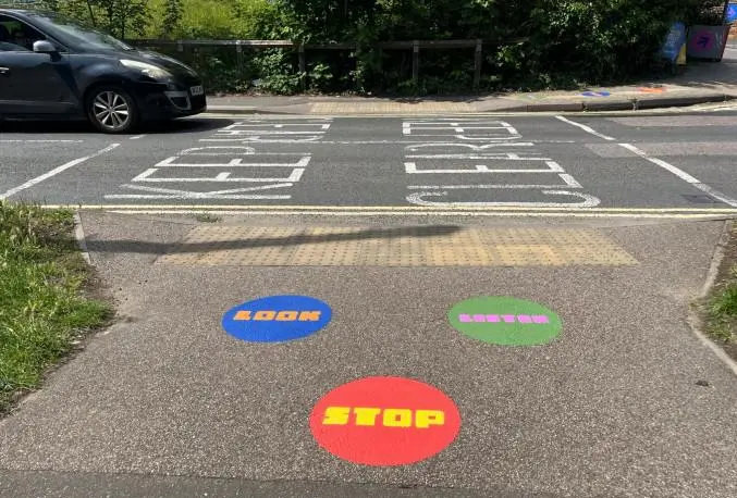 Three round coloured shapes painted on the pavement at a road junction that say Look, Stop and Listen