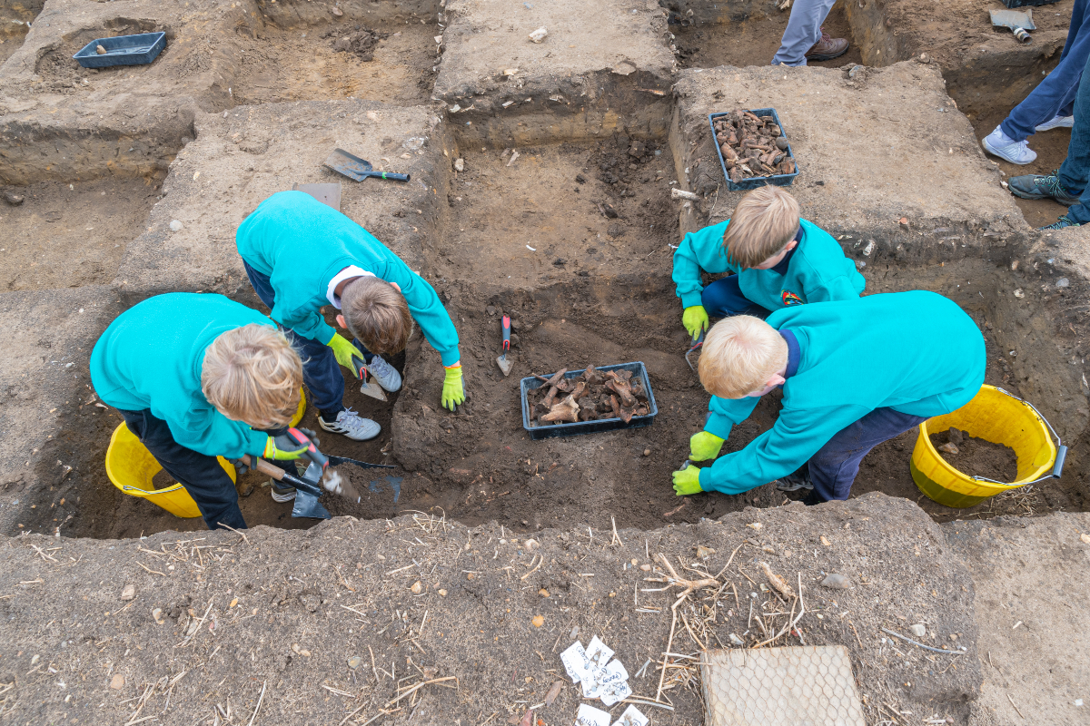 Children from Rendlesham Primary school excavating an Anglo-Saxon rubbish pit, revealing the remains of animal bones at Rendlesham. Summer 2022.