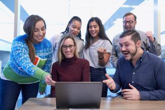 Diverse group of people gathered around a laptop