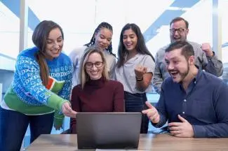Diverse group of people gathered around a laptop