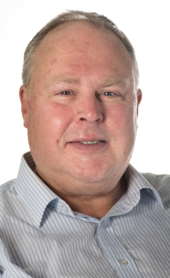 An image of a man wearing a pale grey striped shirt smiling. 