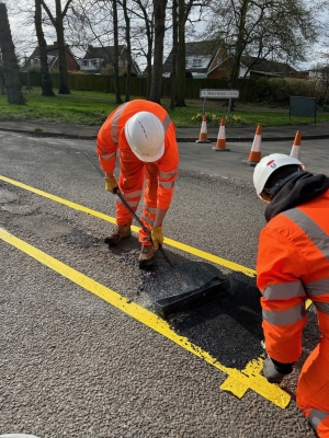 Two people in orange fluorescent clothing mending a road.