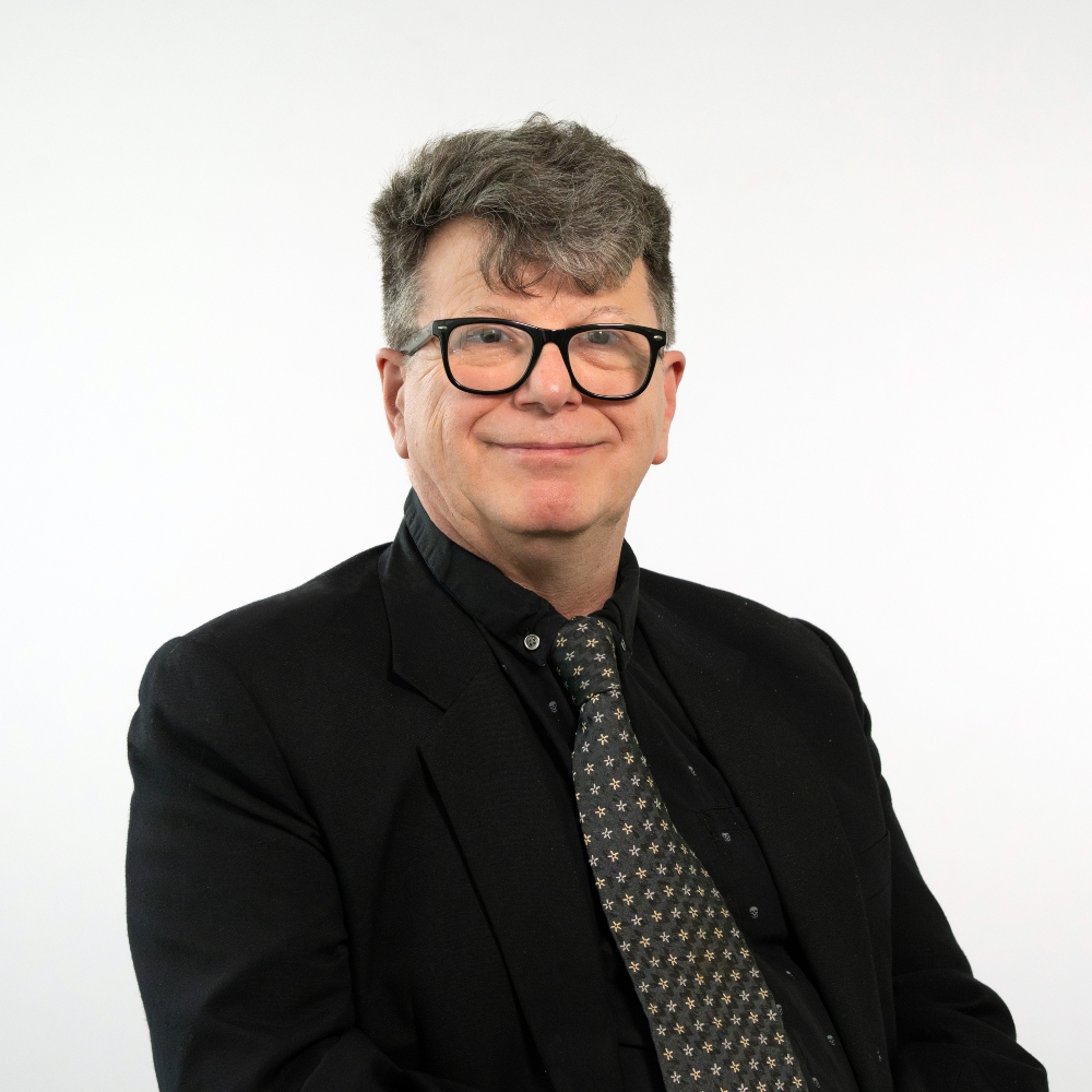 Councillor Robin Baxter-Ayling wearing a black jacket and shirt with a grey patterned tie smiling