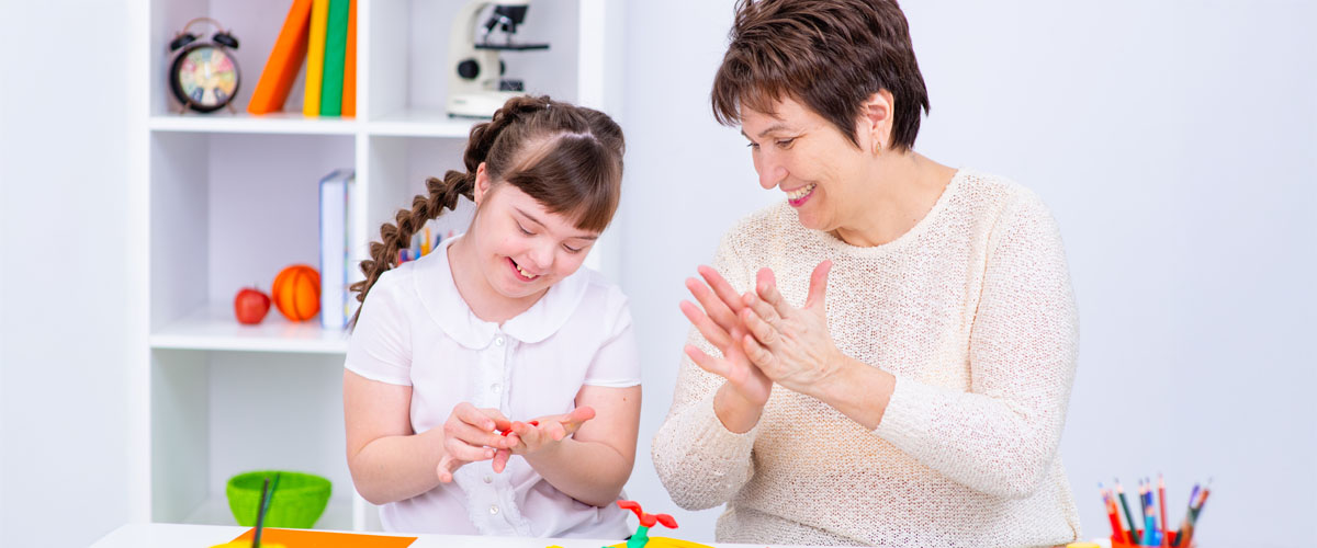 A teacher and young girl are molding play-doh together, they are both happy and smiling.