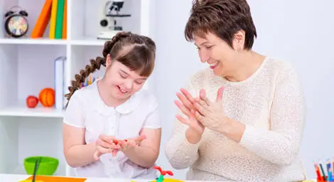 A teacher and young girl are molding play-doh together, they are both happy and smiling.