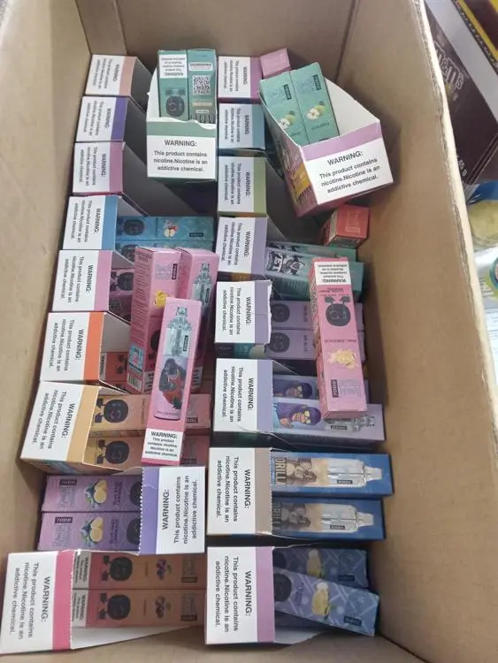 A cardboard box containing multiple vapes in brightly coloured packaging