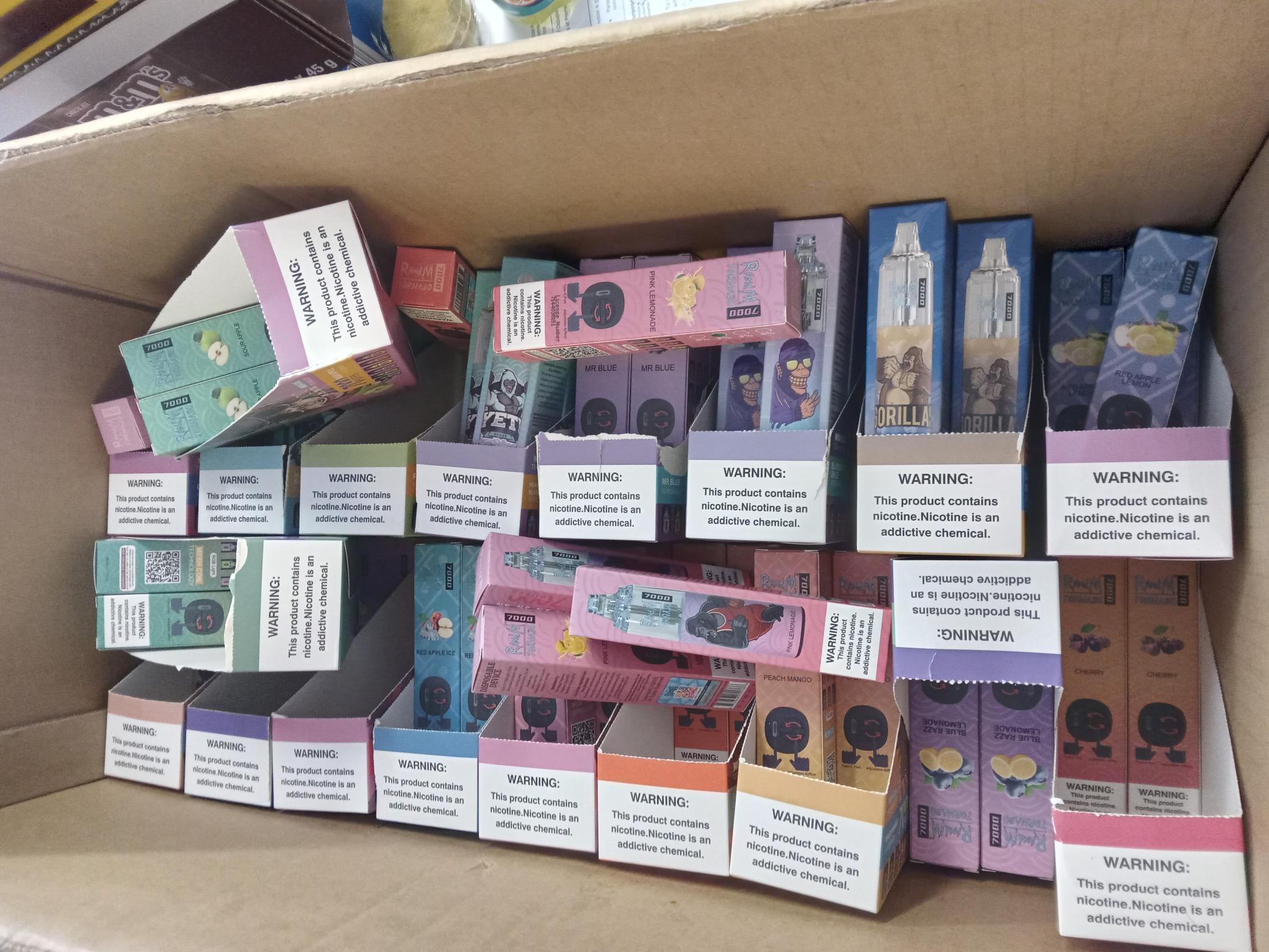 A cardboard box containing multiple vapes in brightly coloured packaging